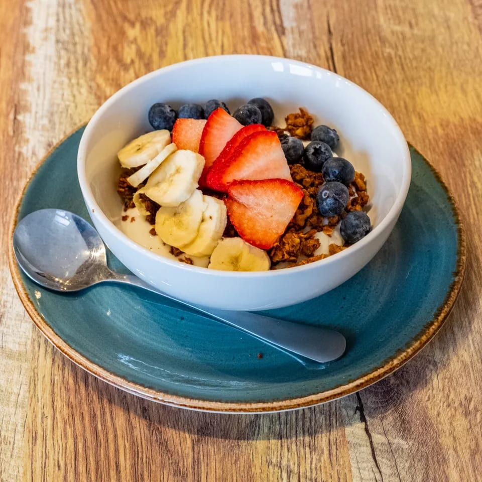 A white bowl of yogurt, granola, sliced bananas, strawberries, and blueberries on a blue plate.