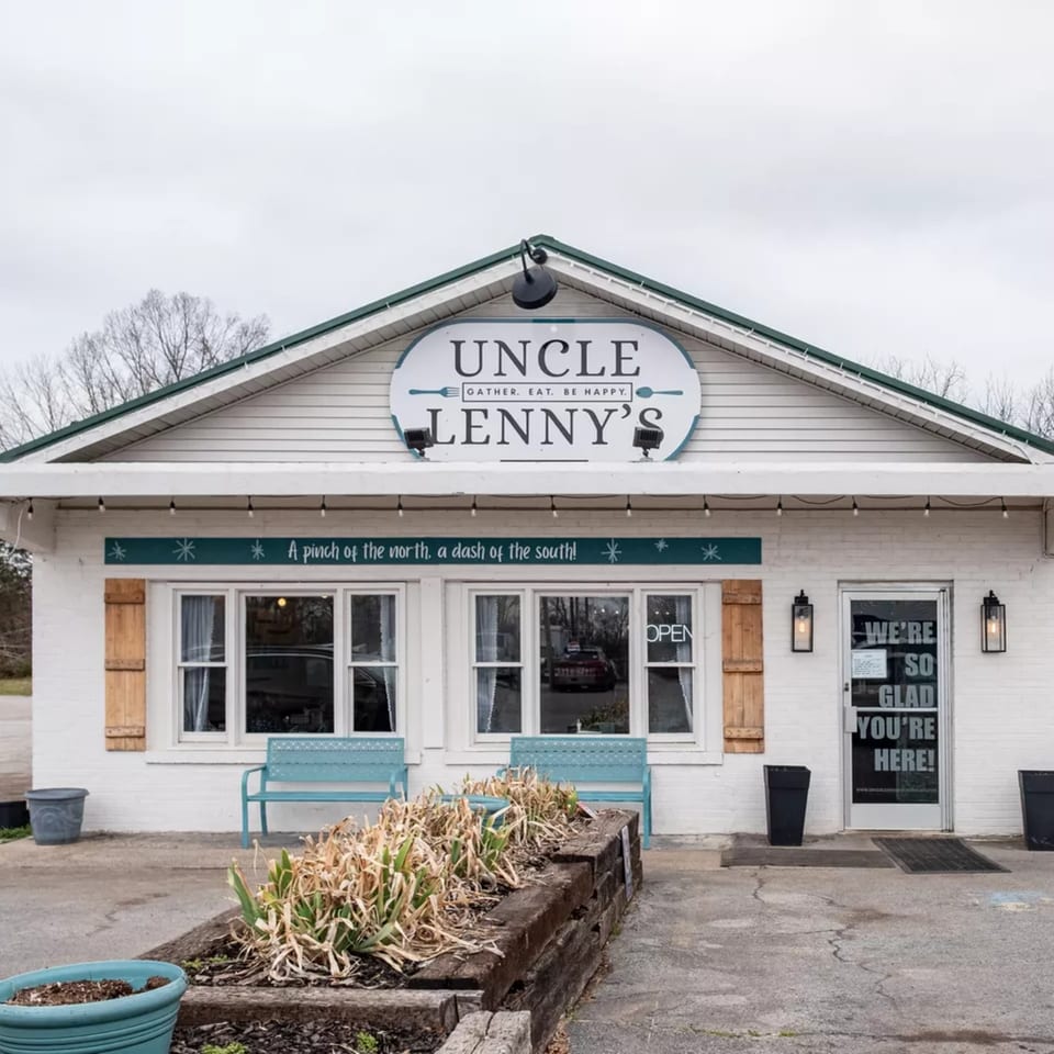 Exterior of Uncle Lenny's Country Cafe, a white building with a green roof and a sign that reads "Gather. Eat. Be Happy."