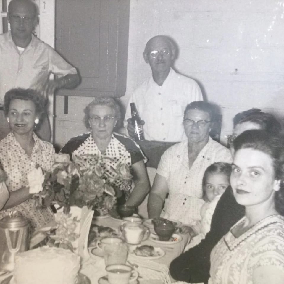 Black and white photo of a family gathered around a table with cake and drinks at Uncle Lenny's.