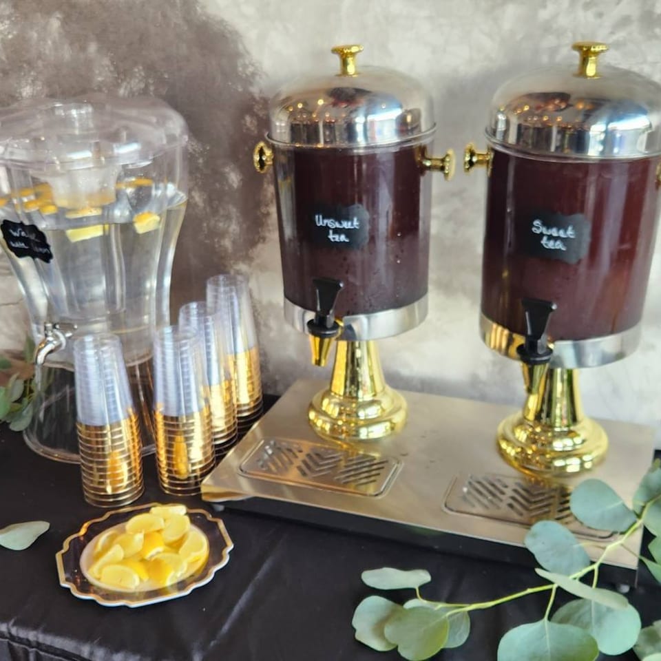 Beverage station with water, sweet tea, unsweet tea dispensers, gold-rimmed cups, and lemon slices.