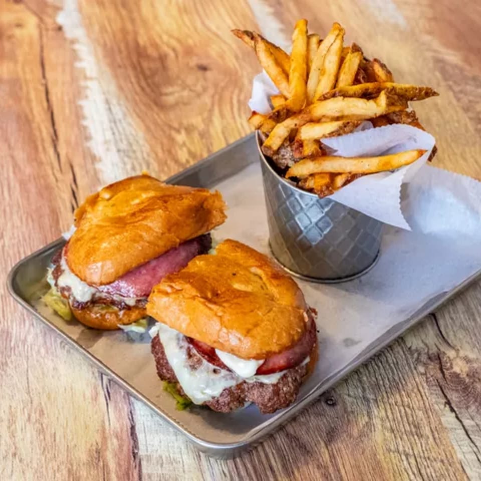 Two burgers with cheese and tomato on a tray with a side of french fries.