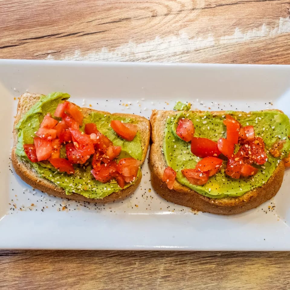 Two slices of avocado toast with diced tomatoes and everything bagel seasoning on a white plate.
