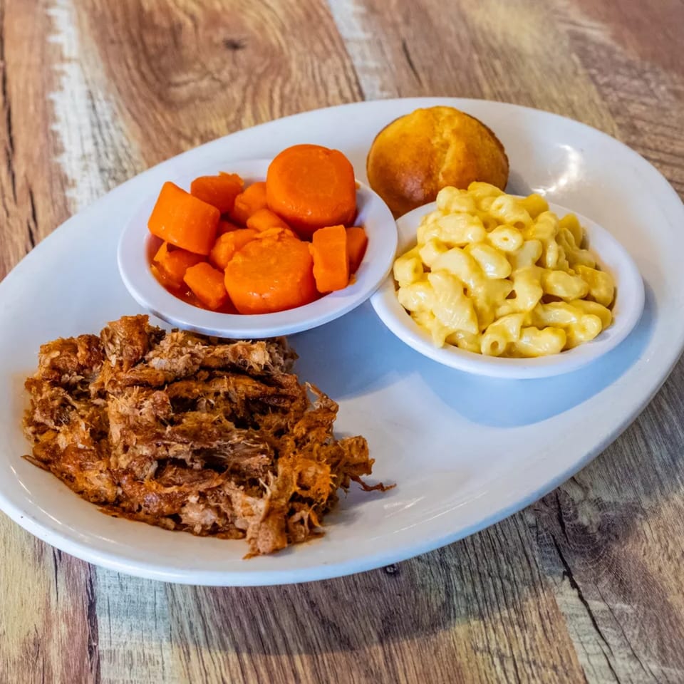 A country cafe meal with pulled pork, candied carrots, macaroni and cheese, and a cornbread muffin.