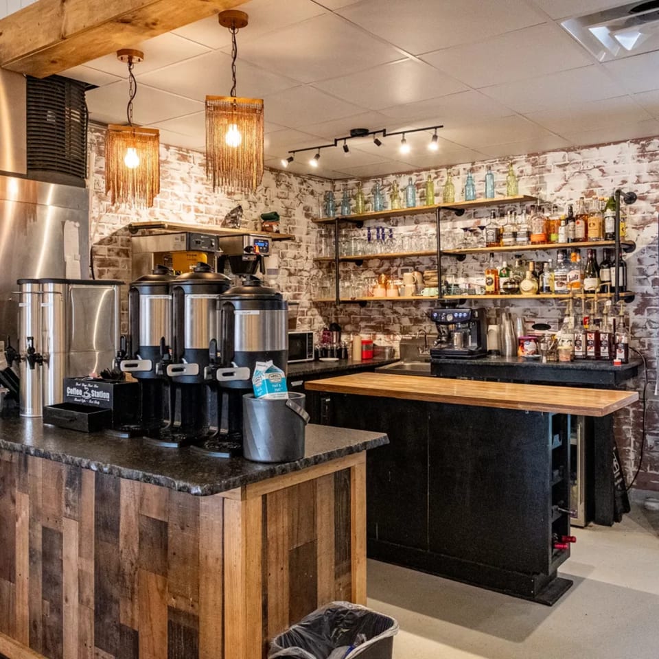 A coffee and beverage station with multiple coffee dispensers, liquor bottles, and glasses on shelves.