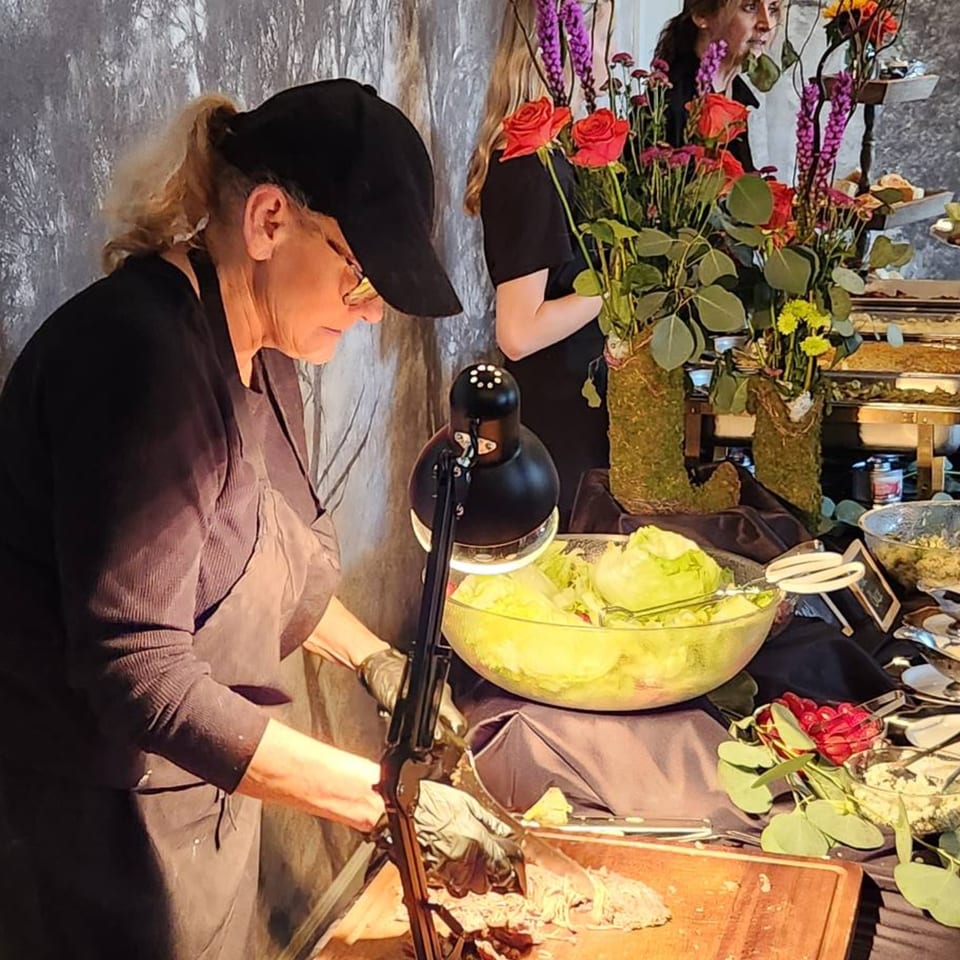 A caterer carves meat at a buffet table with salads and floral arrangements.