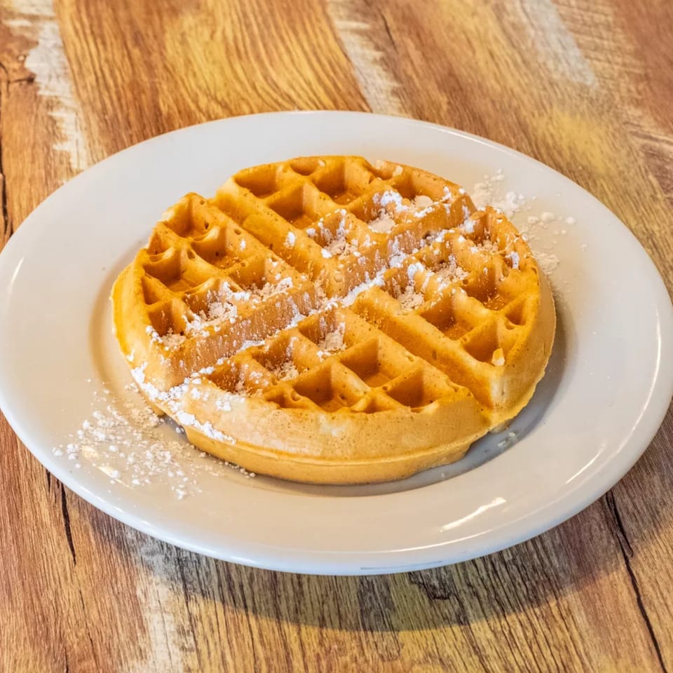 A golden-brown waffle dusted with powdered sugar on a white plate at Uncle Lenny's Country Cafe.