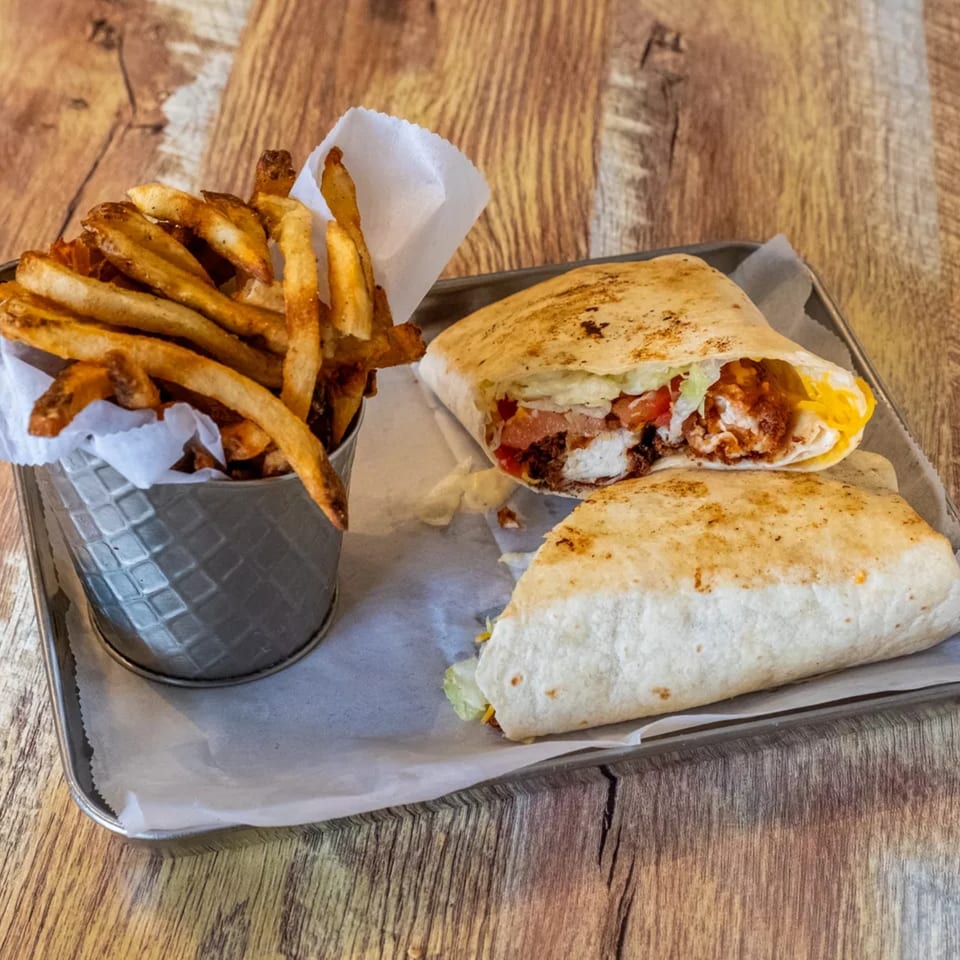 A chicken wrap, cut in half, with a side of crispy fries in a metal cup on a tray.